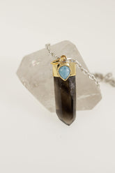 Smoky Phantom Quartz Larimar pendant displayed on Clear Quartz with gold-plated sterling silver cap and blue cabochon.