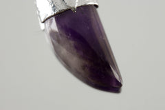 Close up of Tooth Shaped Amethyst Cabochon Stack Pendant shown on light background.