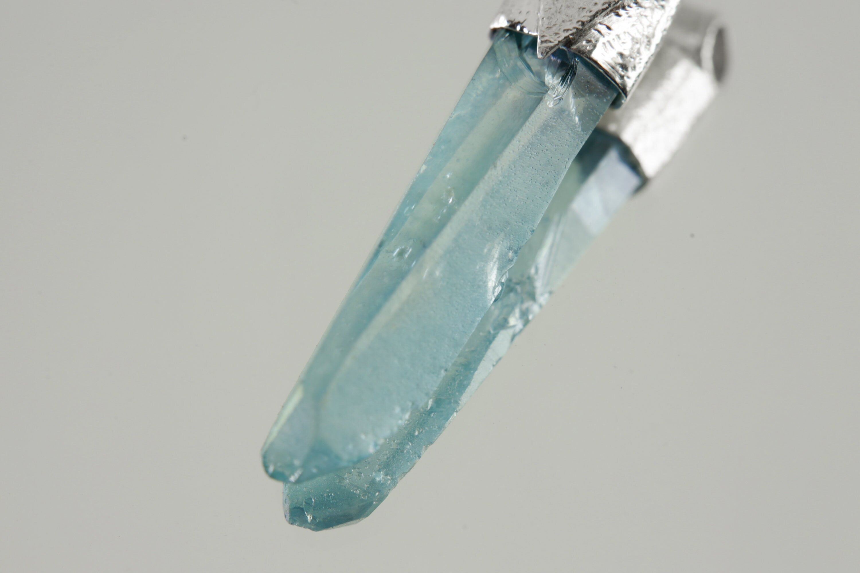 Close-up of Lemurian Laser Aqua Aura Quartz showing aqua-blue bonded surface, crystal point, and textured silver cap.