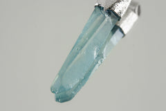 Close-up of Lemurian Laser Aqua Aura Quartz showing aqua-blue bonded surface, crystal point, and textured silver cap.