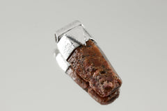 Hexagonal Ruby Stack Pendant shown on light background with raw red corundum specimen and textured silver cap.