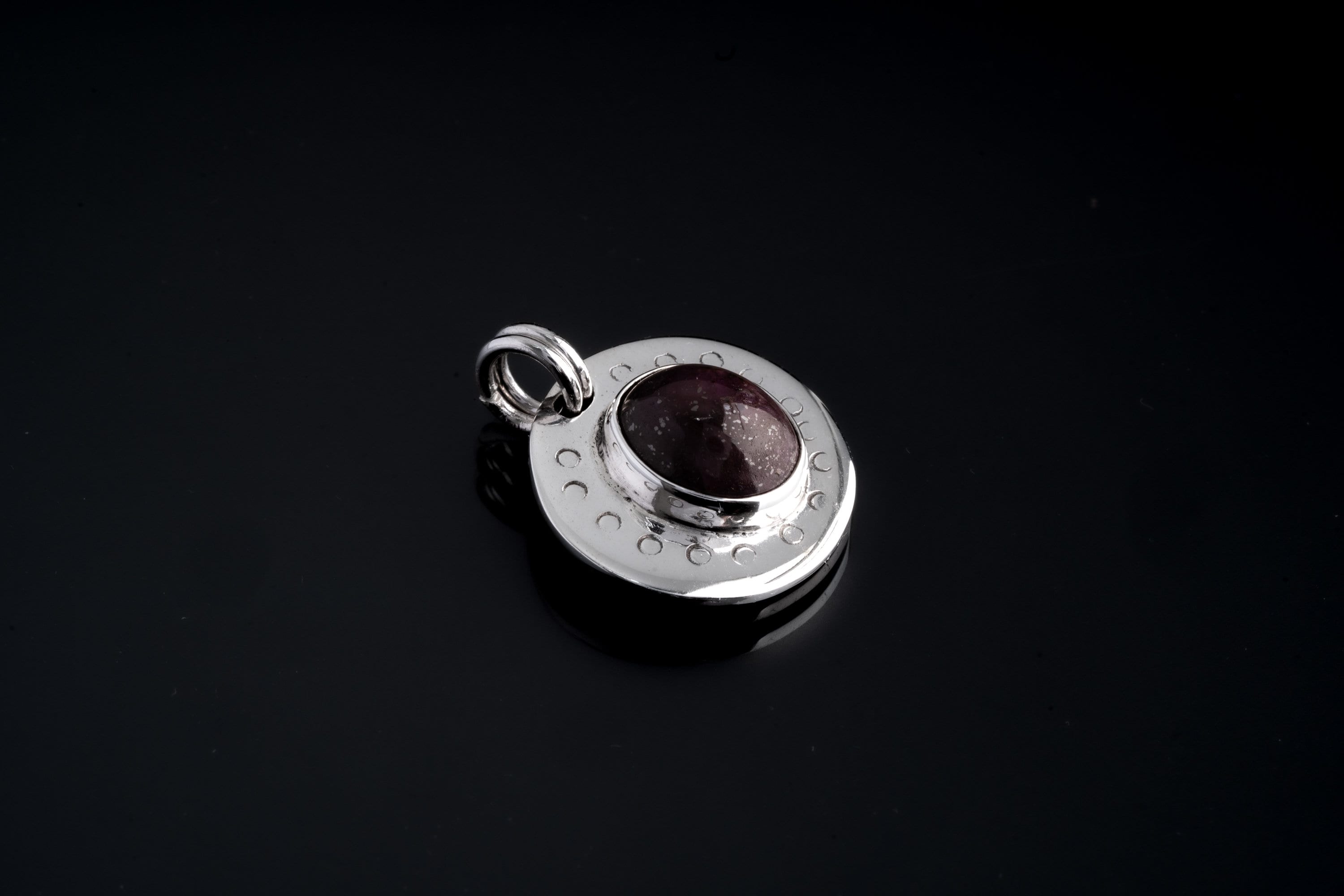 Close-up of Ruby Cabochon pendant on black background, showing polished sterling silver crescent texture and twin round bails.