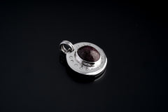 Close-up of Ruby Cabochon pendant on black background, showing polished sterling silver crescent texture and twin round bails.