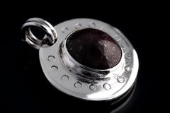 Macro detail of oval Ruby Cabochon set in polished sterling silver, with crescent moon engravings around the circular pendant face.