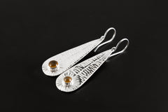 Leaf-shaped sterling silver earrings shown on a dark background with polished botanical texture and round Orange Agate stones.