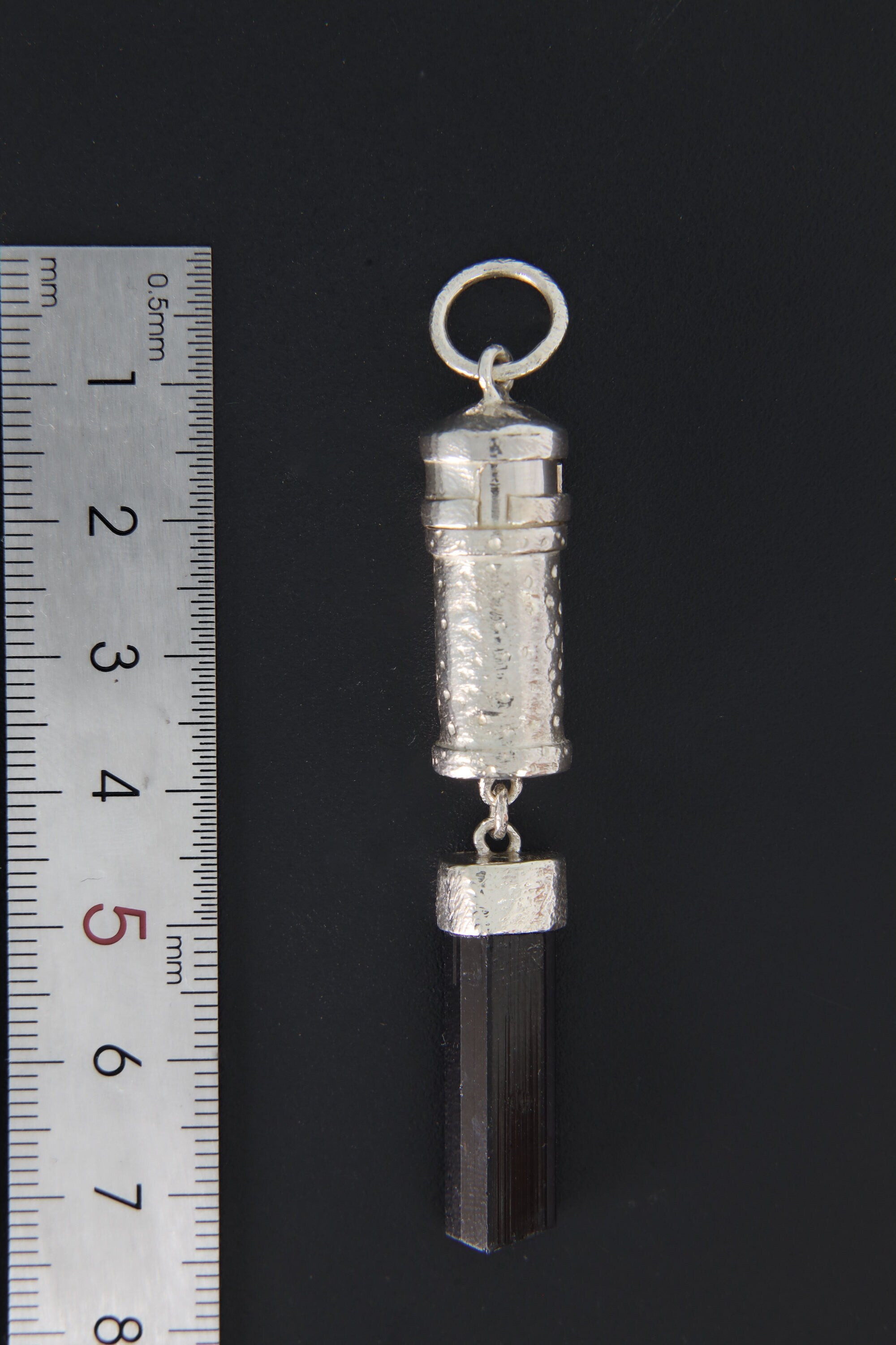 Black Tourmaline sterling silver capsule pendant shown beside a ruler for scale, with raw crystal base and round bail.
