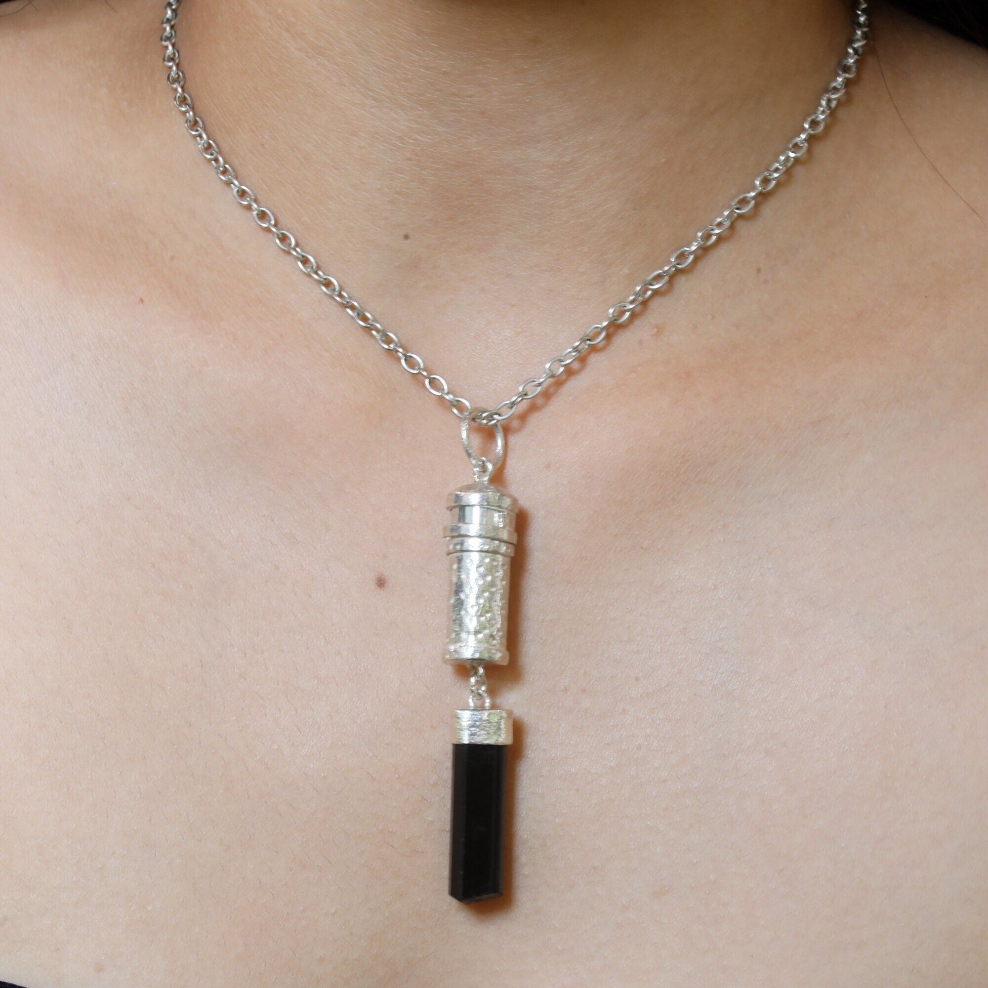 Black Tourmaline sterling silver capsule pendant worn on a model, showing polished silver locket and raw black crystal drop.