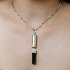 Black Tourmaline sterling silver capsule pendant worn on a model, showing polished silver locket and raw black crystal drop.