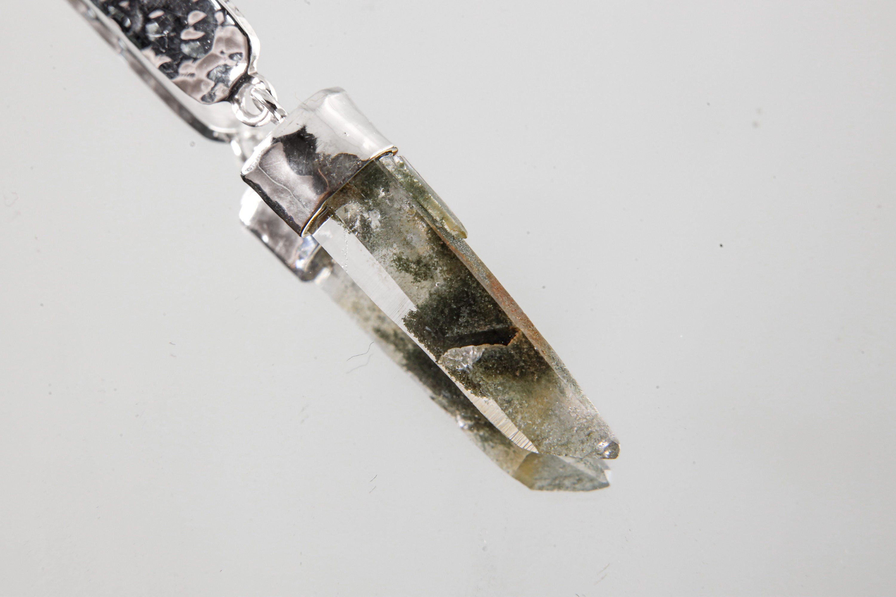 Close-up of Himalayan Chlorite Inclusion Quartz point suspended below shiny hammered sterling silver plate.