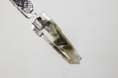 Close-up of Himalayan Chlorite Inclusion Quartz point suspended below shiny hammered sterling silver plate.