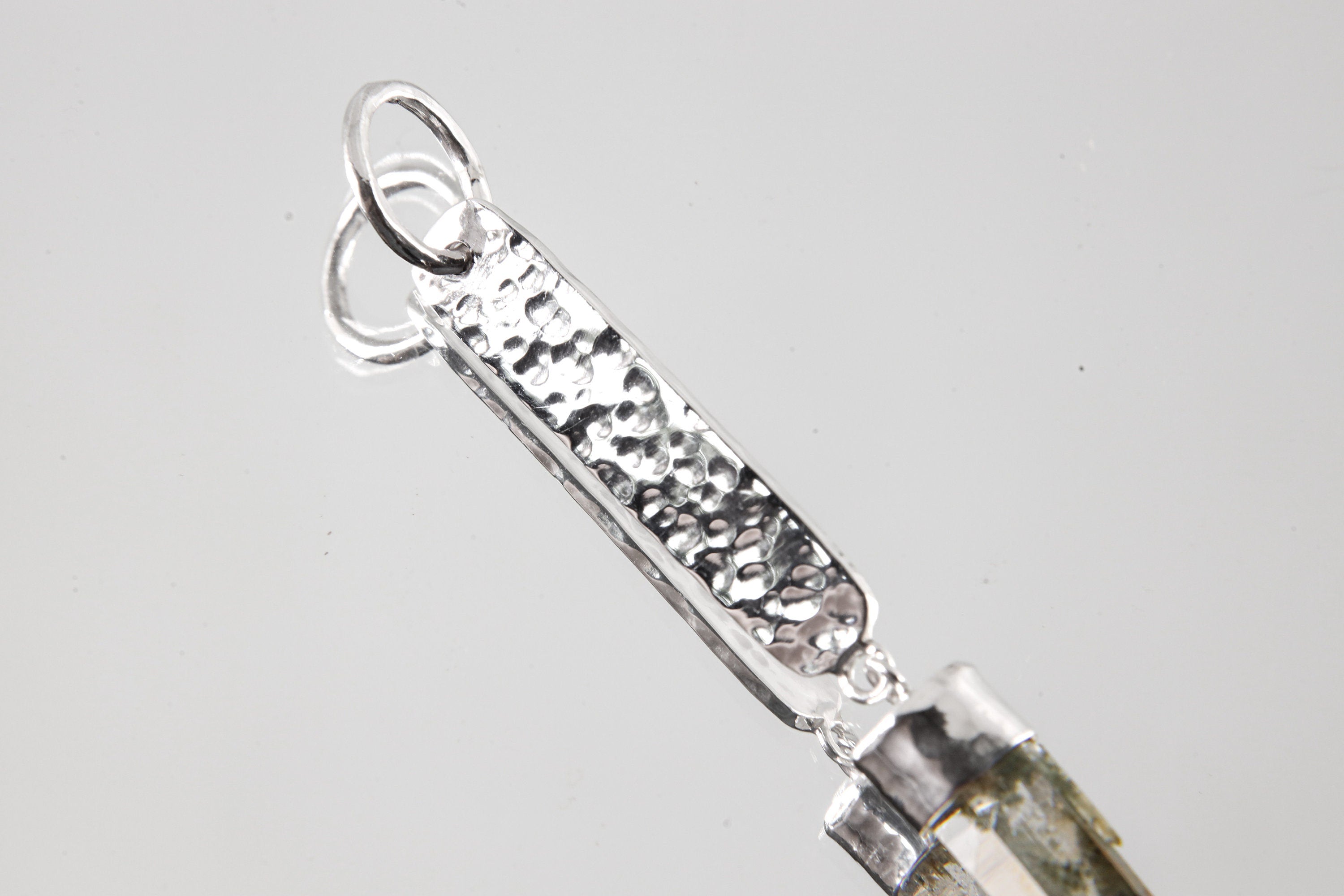Close-up of hammered sterling silver pendant showing bright texture, round bail, and handmade silver detail.
