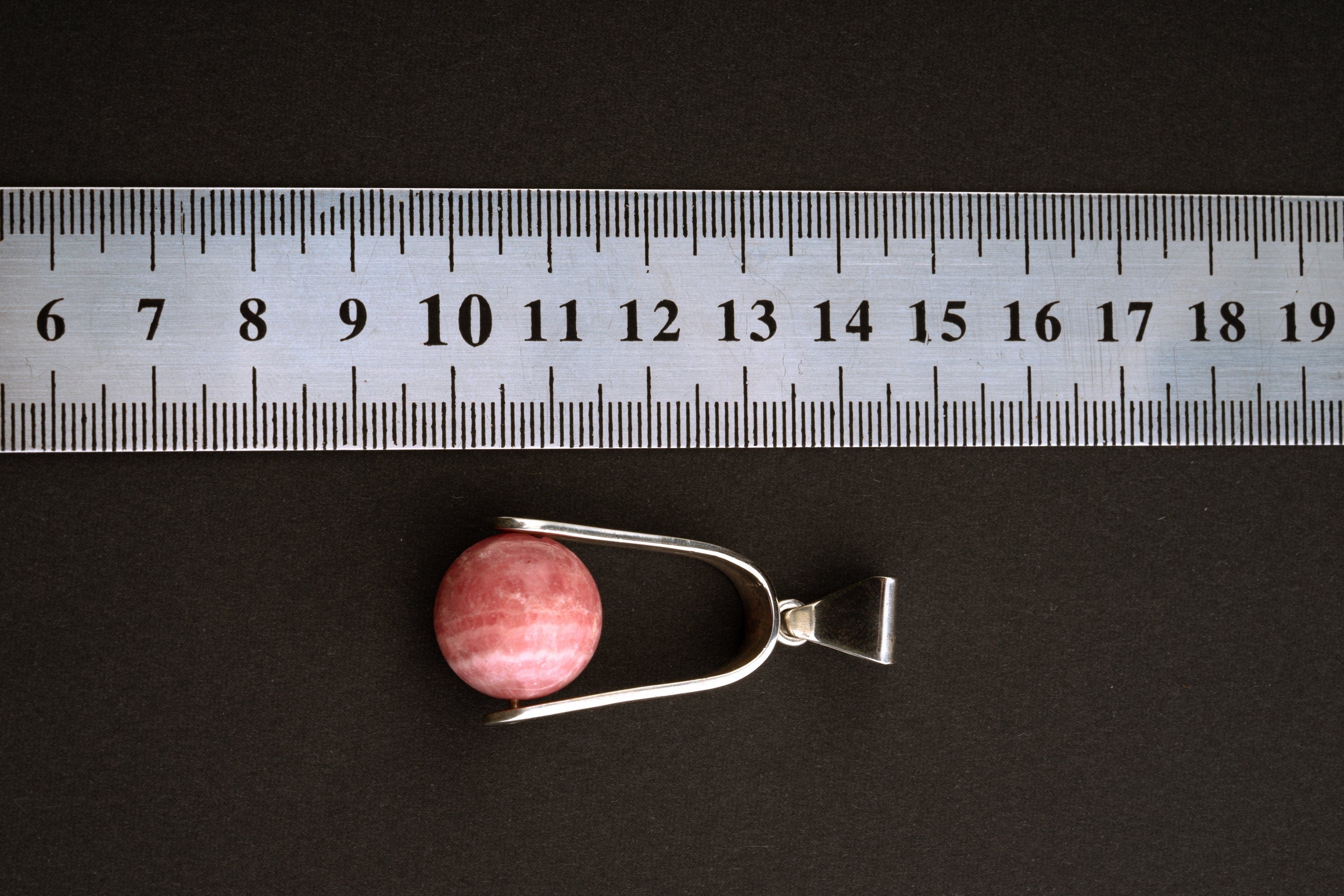 Rhodochrosite spinning pendant shown beside a ruler for scale, measuring approximately 5 cm by 2 cm.