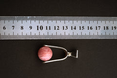 Rhodochrosite spinning pendant shown beside a ruler for scale, measuring approximately 5 cm by 2 cm.