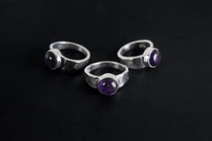 Group of Harmonious Amethyst Essence Rings shown on black background with hammered sterling silver bands and purple stones.