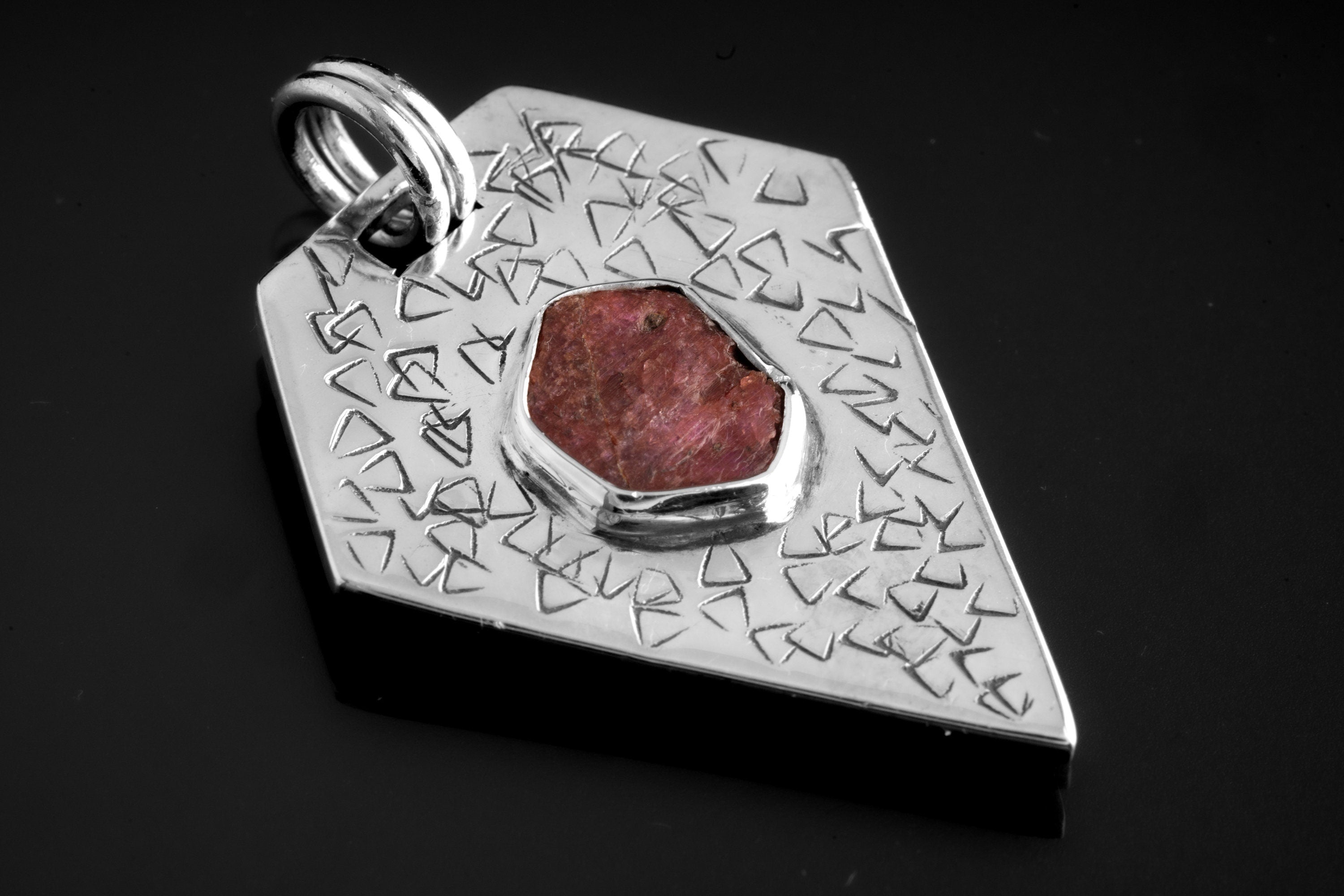 Geometric Ruby pentagon pendant in oxidized 925 sterling silver, shown on black with abstract texture and central red stone.