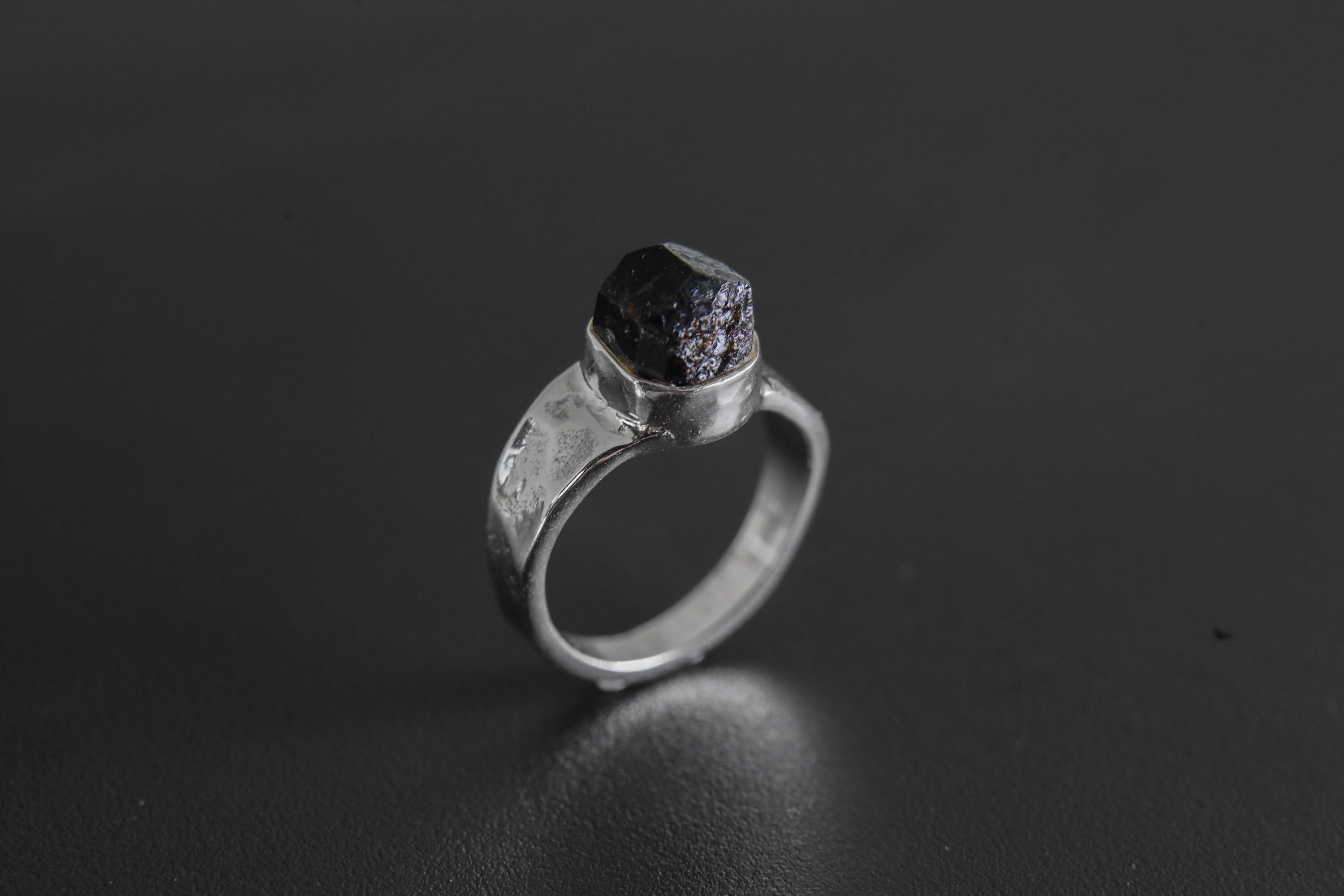 Handmade 925 sterling silver Black Tourmaline ring shown on a dark background, with raw black crystal and hammered silver band.