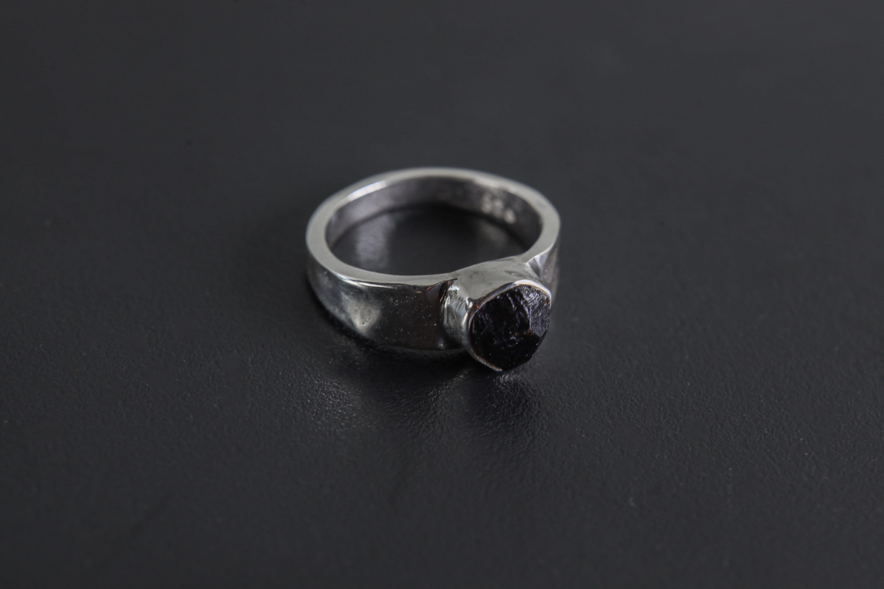 Handmade 925 sterling silver Black Tourmaline ring shown on a dark background, with raw black crystal and hammered silver band.