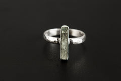 Long square cut Aquamarine ring displayed on clear quartz, showing polished silver band and vertical blue gemstone setting.