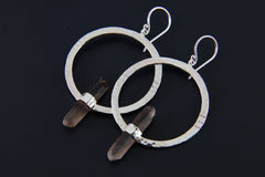 Smoky Quartz hoop earrings shown on a dark background with large circular silver frames and raw crystal dangles.