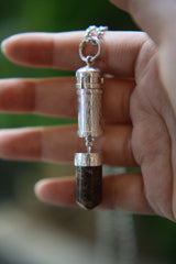 Brown Tourmaline capsule pendant held in hand, showing sterling silver locket shape and polished Dravite point.