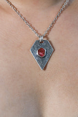 Ruby pentagon pendant shown worn on the chest, with textured sterling silver and deep red gemstone centre.