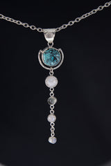 Round Turquoise orb pendant shown on a black background, with textured sterling silver frame and Moonstone dangles.