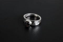 Crimson Sentinel Garnet Ring shown on black background with deep crimson stone and high-shine silver band.