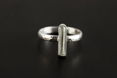 Aquamarine sterling silver ring shown on a dark background, with long vertical blue gemstone and hammered silver band.