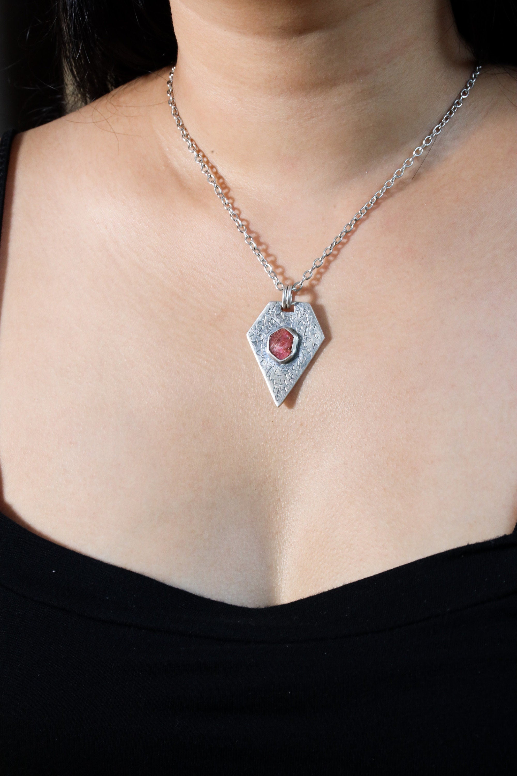 Ruby pentagon pendant shown worn on a model, with oxidized sterling silver texture and bold geometric shape.