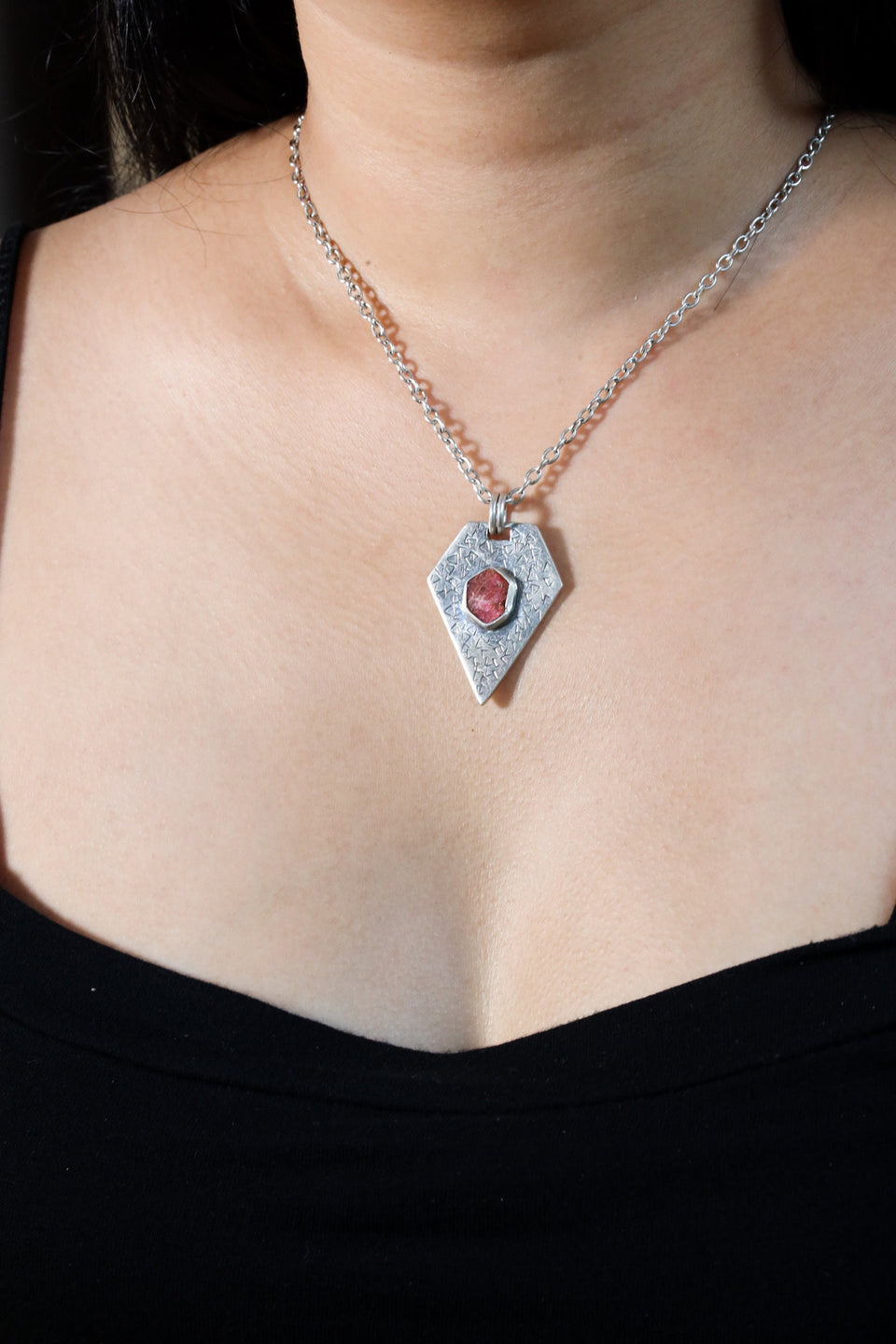 Ruby pentagon pendant shown worn on a model, with oxidized sterling silver texture and bold geometric shape.