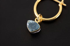 Close-up of Blue Tourmaline hoop earring pendant showing Indicolite slice and polished gold-plated setting.