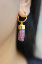 Ruby gold-plated sterling silver hoop earring worn on a model as a single dangle crystal charm.