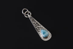 Ocean Whisper Larimar pendant shown on dark background with polished hammered sterling silver and blue teardrop stone.