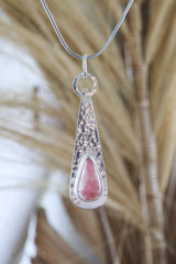 Rhodochrosite sterling silver pendant shown on a necklace with hammered silver texture and pink teardrop gemstone.