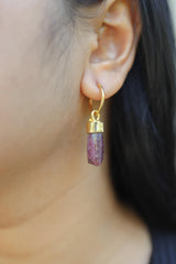 Golden Ruby Flame earring pendant worn on a model, showing gold hoop and red crystal dangle.