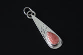 Rhodochrosite teardrop pendant shown on dark background with hammered sterling silver and pink gemstone centre.