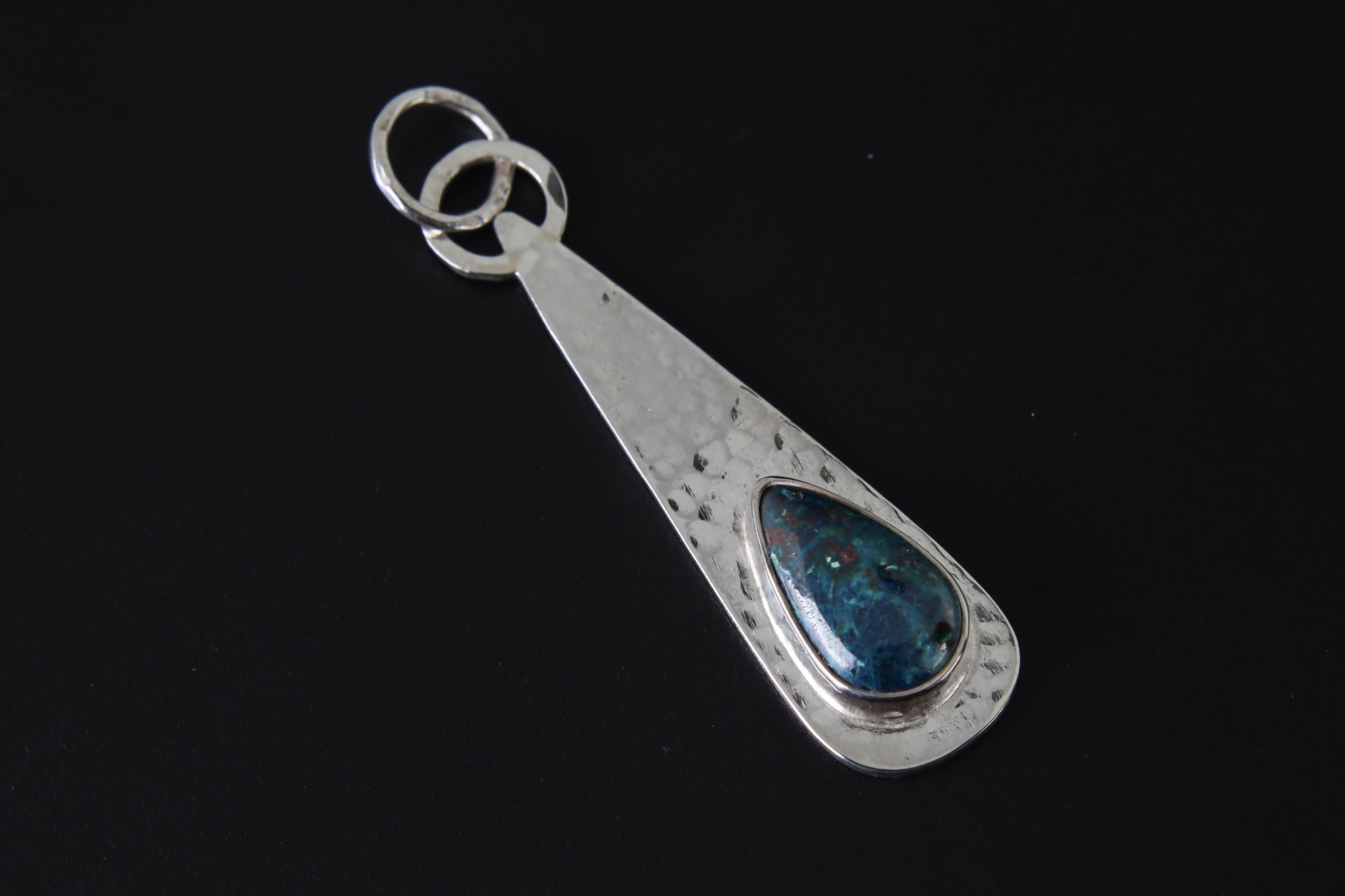 Rhodochrosite teardrop pendant shown on dark background with hammered sterling silver and pink gemstone centre.