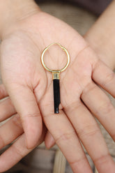 Black Tourmaline gold-plated hoop earring held in hand, showing single-piece convertible charm design.