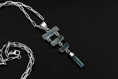 Raw Aquamarine cascade pendant in 925 sterling silver with four blue stones, open-back bezels, and a black necklace cord.