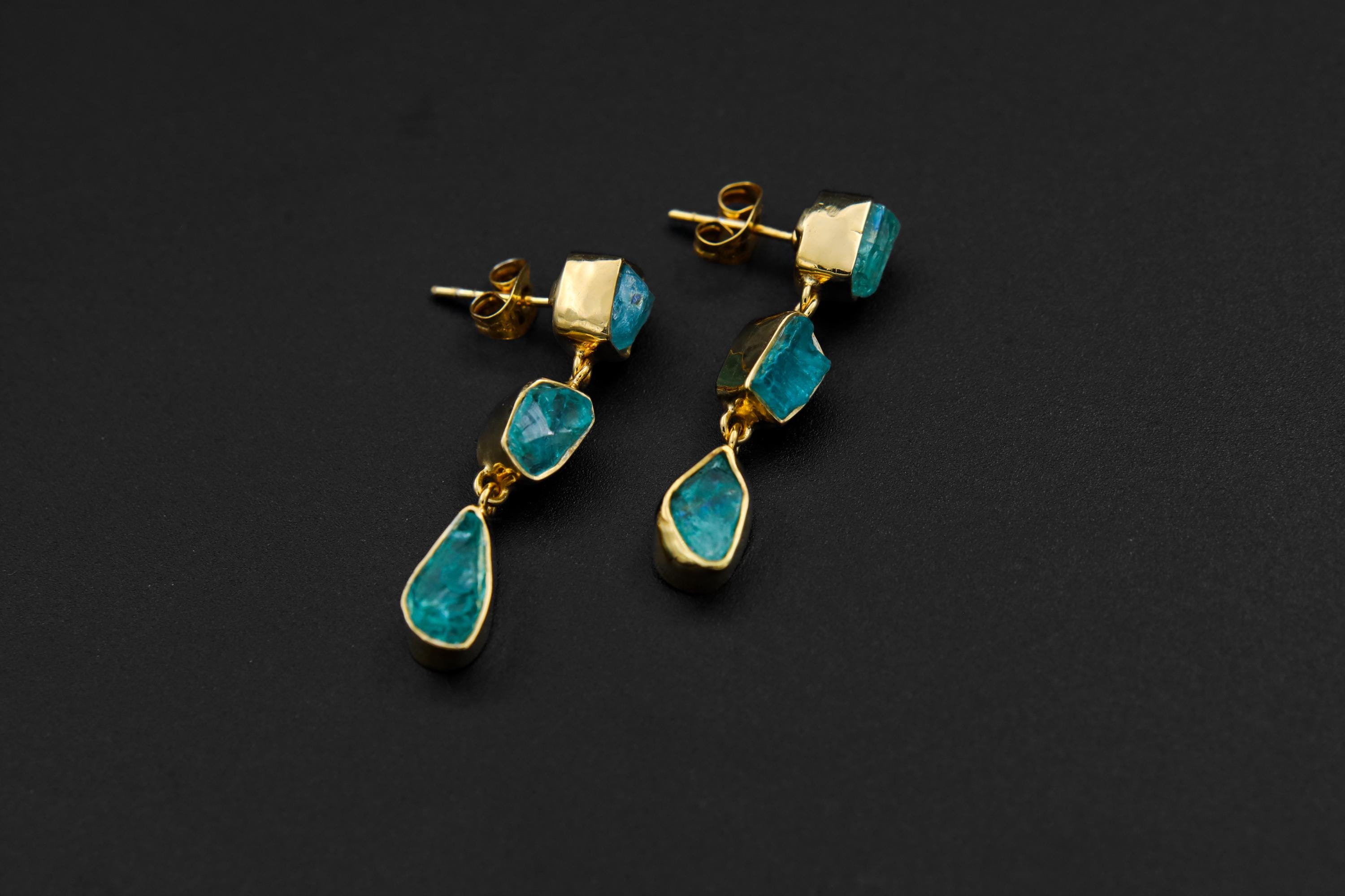 Handmade 18k gold-plated 925 sterling silver Blue Apatite drop earrings shown on a dark background, with raw blue stones and teardrop crystal dangles.
