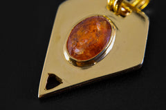 Close-up of Red Kyanite slice pendant showing faceted orange-red mineral surface, gold-plated setting, and geometric form.