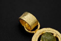 Close-up of raw Peridot pendant showing green crystal texture, sand-textured gold-plated setting, and wide bail.