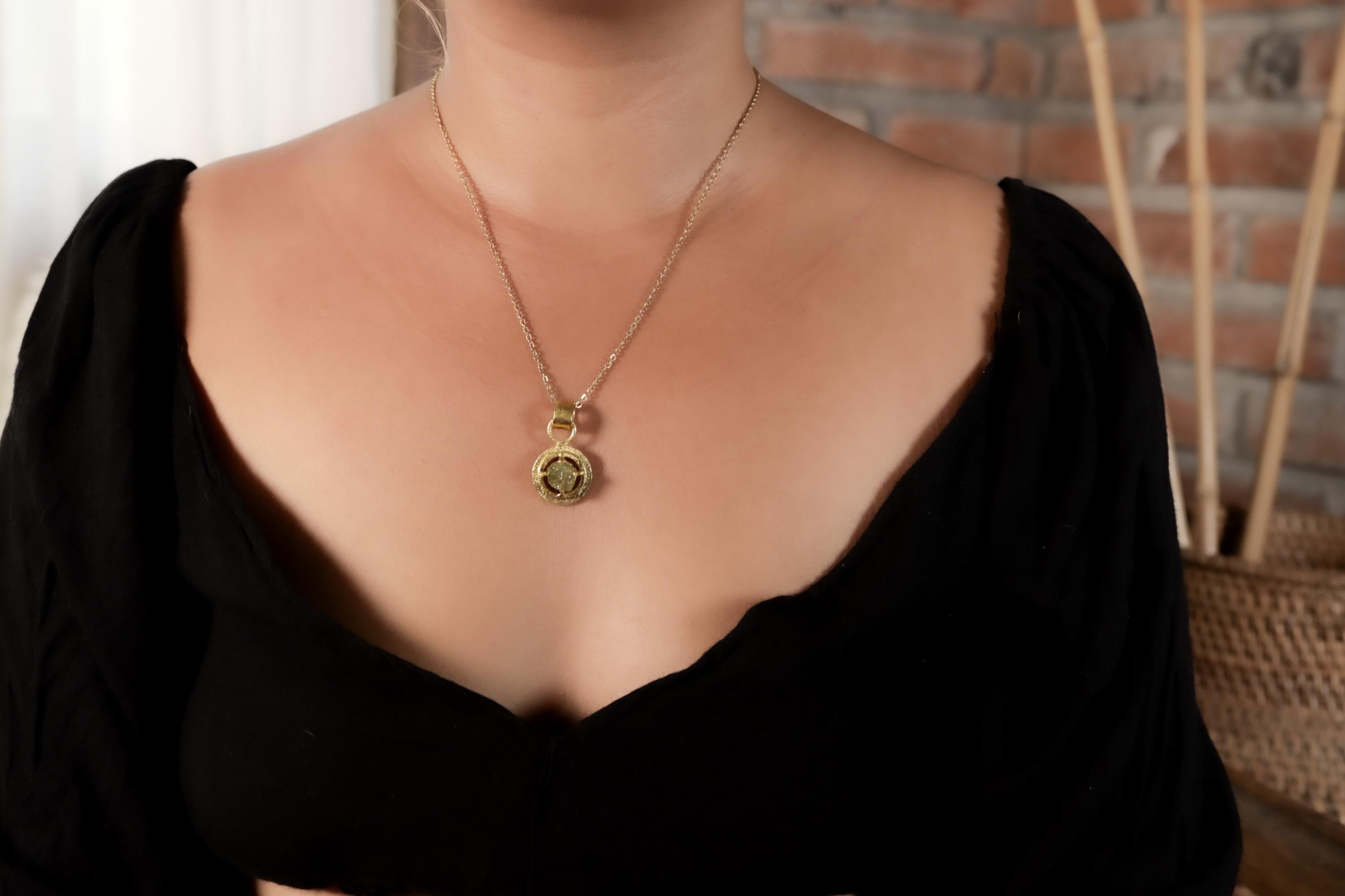 Raw Peridot pendant shown worn on a necklace, with 18k gold-plated claw frame and compact green gemstone shape.