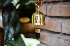 Smoky Quartz Gold Plated Prayer Bell hanging near brick wall with warm golden shine and dark crystal point.