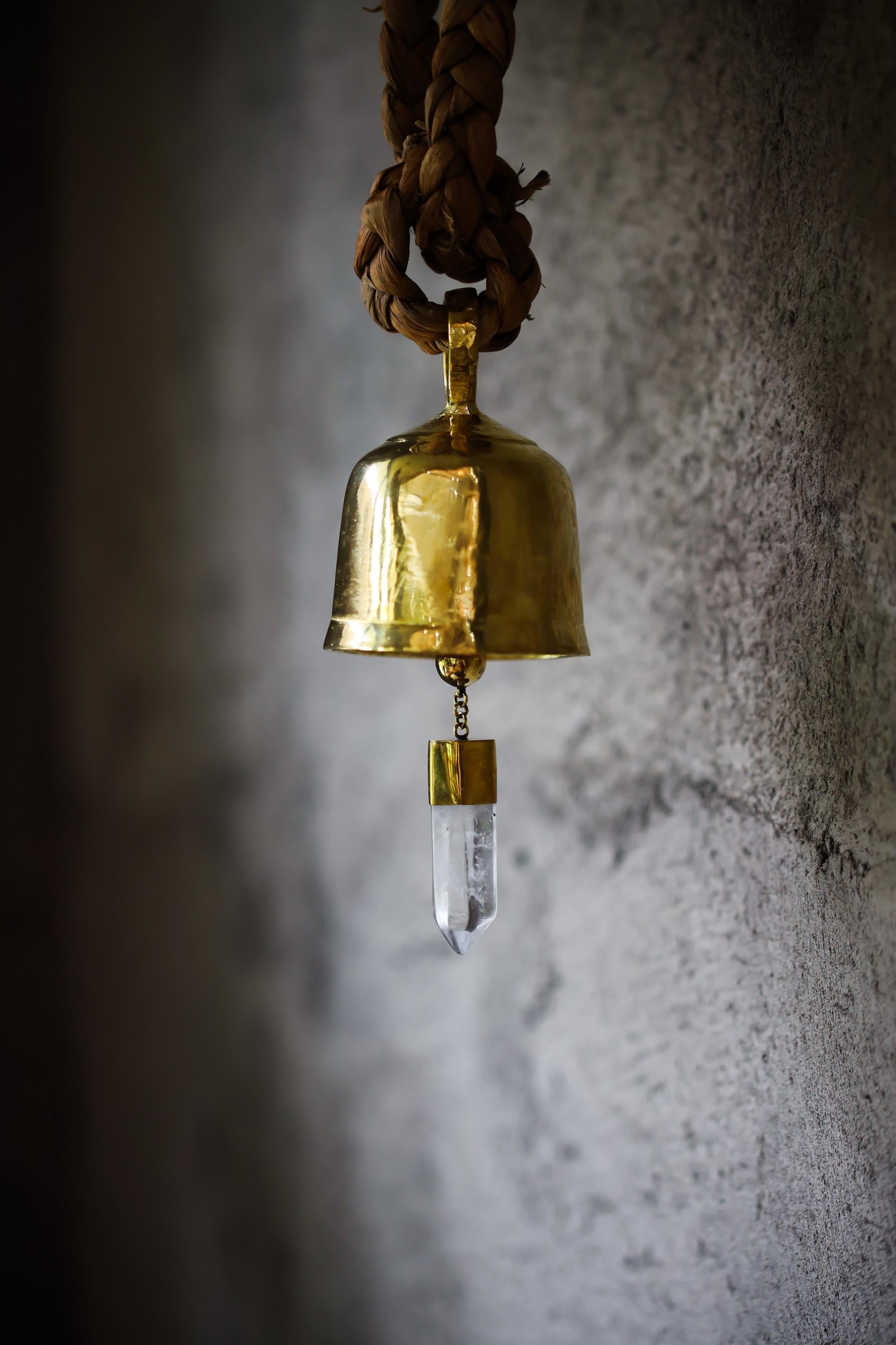 Clear Quartz Gold Plated Prayer Bell hanging against a textured wall with 18k gold-plated bronze and crystal point.