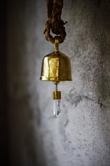 Clear Quartz Gold Plated Prayer Bell hanging against a textured wall with 18k gold-plated bronze and crystal point.