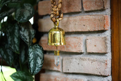 Clear Quartz prayer bell hanging against brick wall with gold-plated bronze finish and crystal detail.