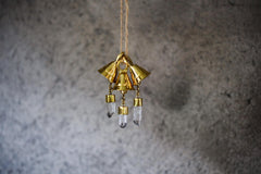 Tiny Clear Quartz prayer bell hanging against a grey wall with 18k gold-plated bronze shine.