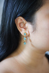 Blue Apatite golden drop earrings shown worn on the ear, with vivid blue gemstones and dangling teardrop crystals.