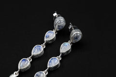 Close view of Blue Moonstone earrings showing teardrop gemstones, organic sterling silver bezels, and luminous blue flash.